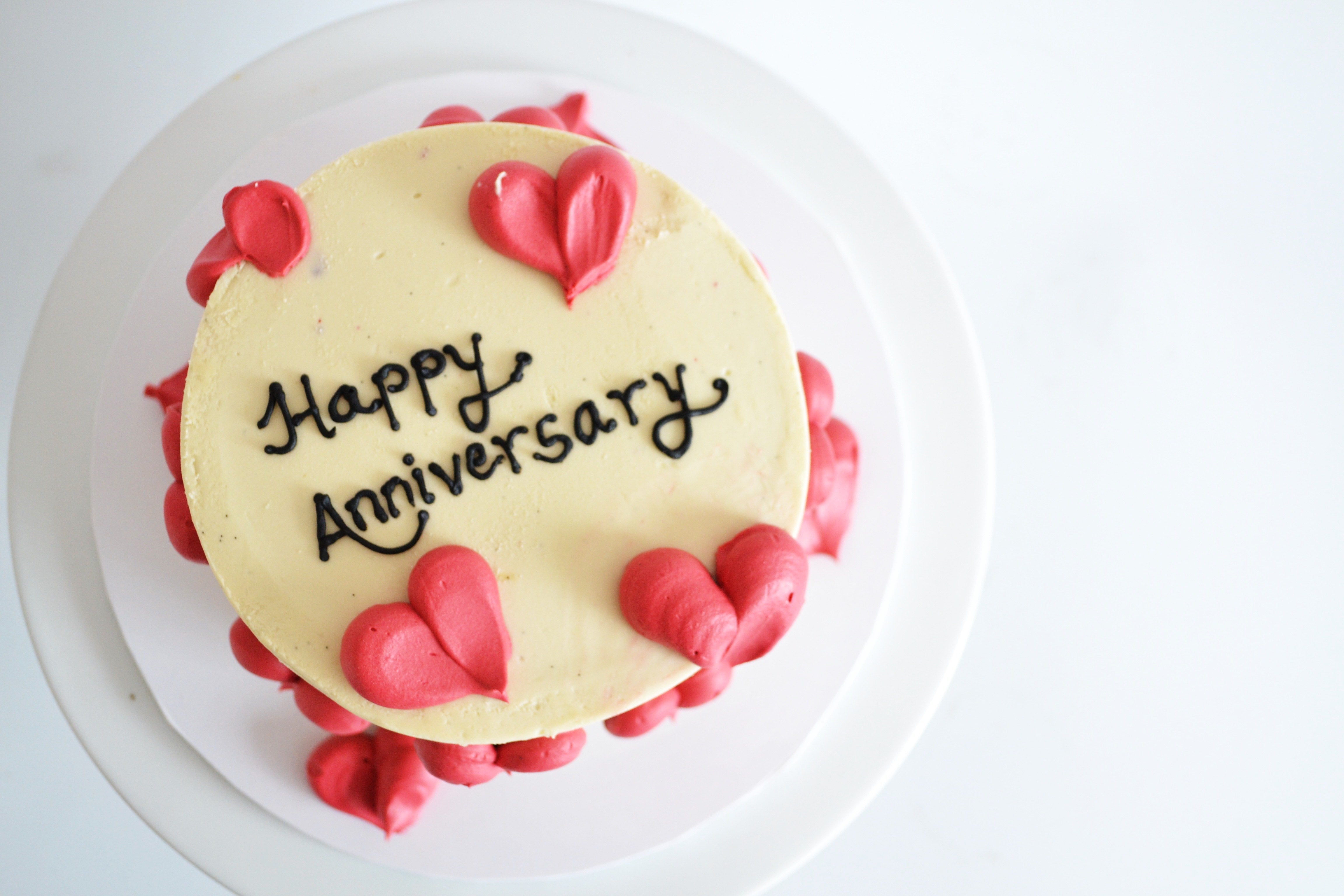 Cake with 'Happy Anniversary' text and red heart decorations on a white background