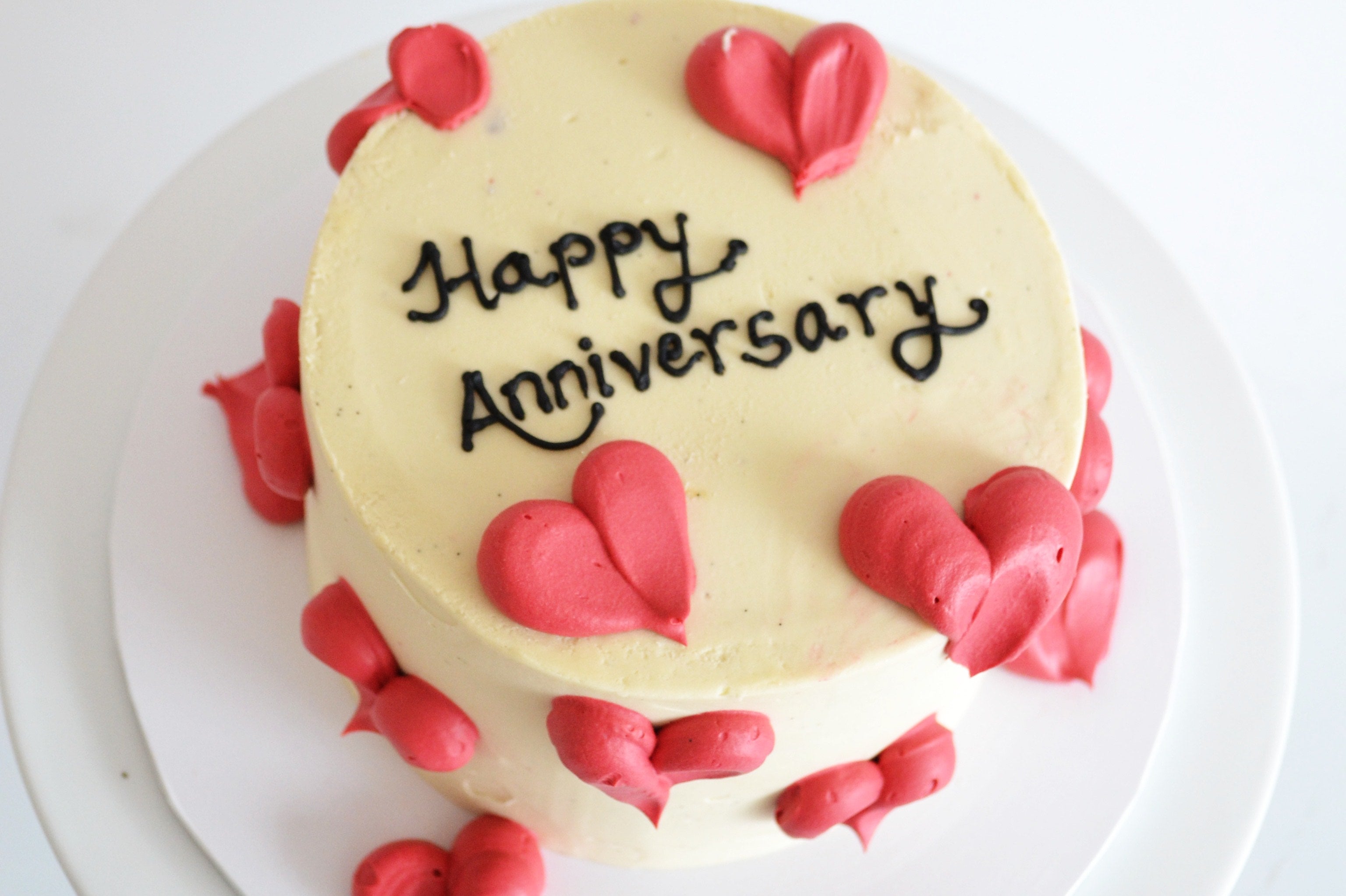 Small round cake with 'Happy Anniversary' text and red heart decorations on a white plate.