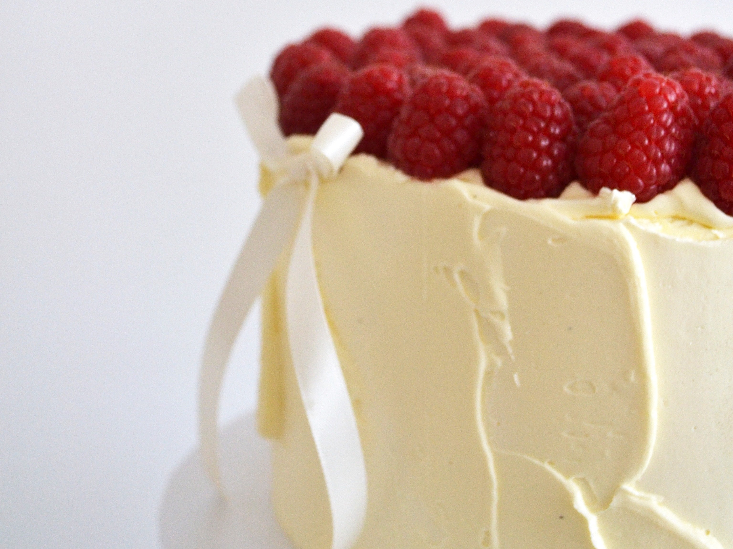Cake with white frosting and raspberries on a white background