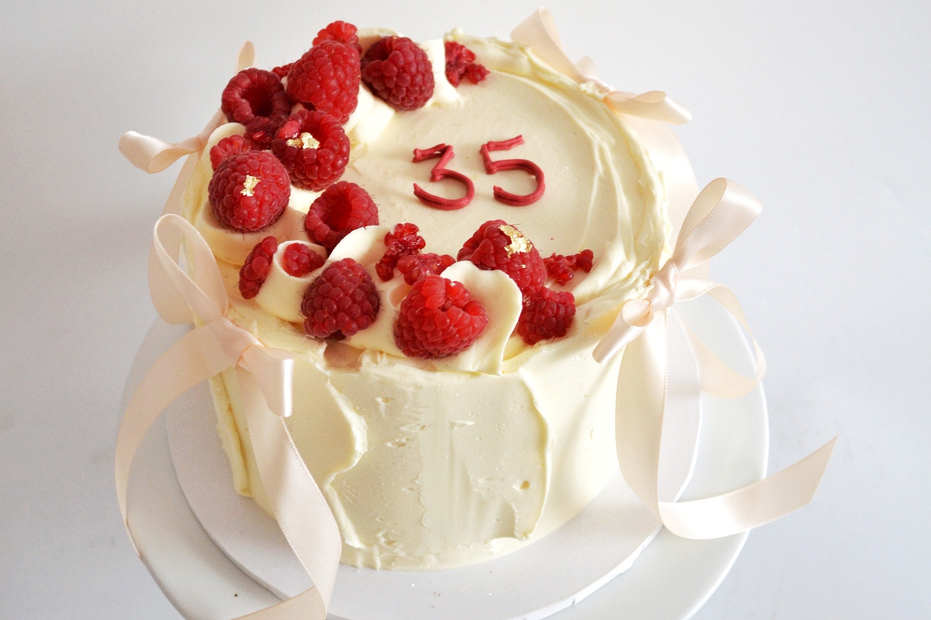 White cake with raspberries and number '35' on a white background