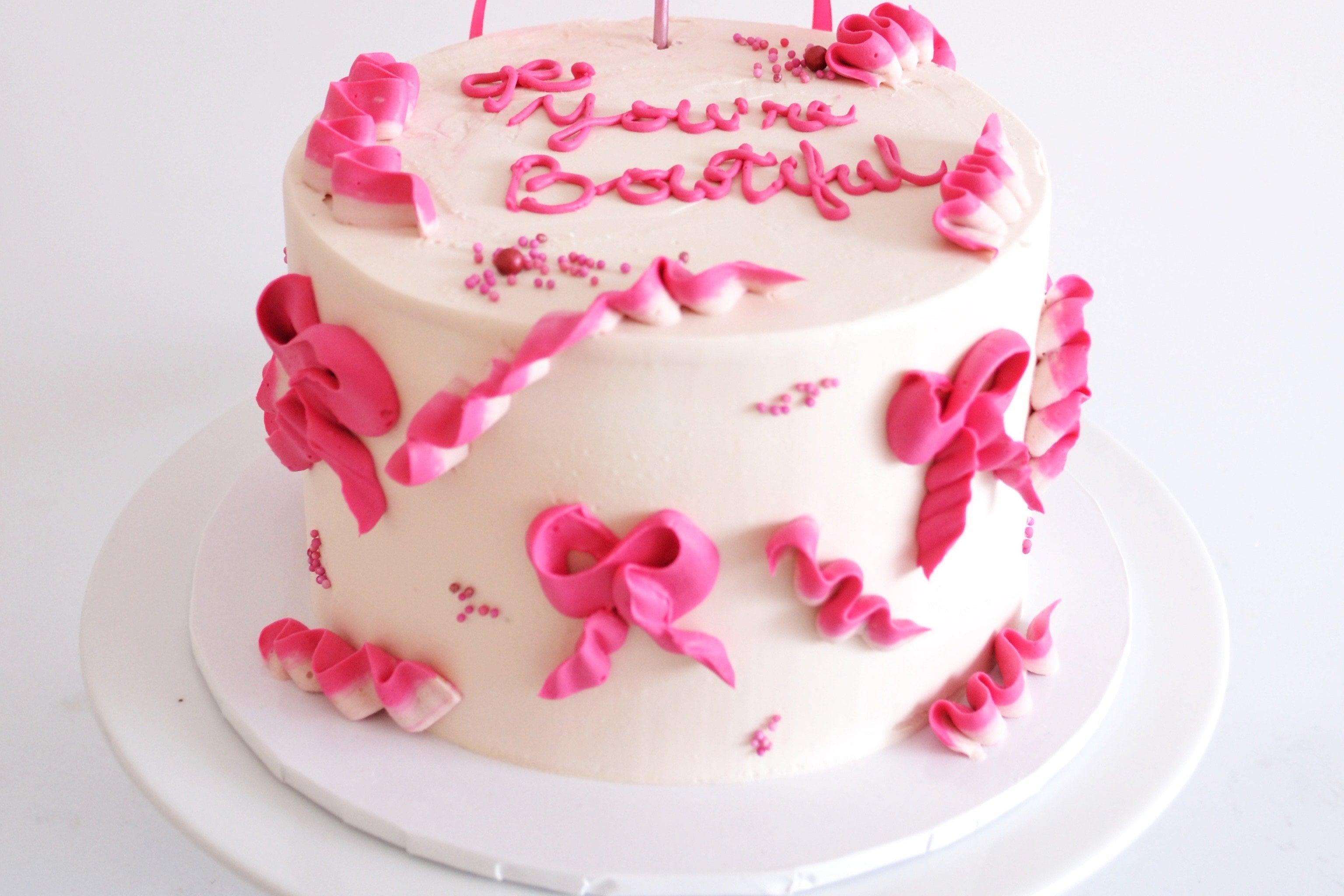 White birthday cake with pink decorations and a pink bow on a white background